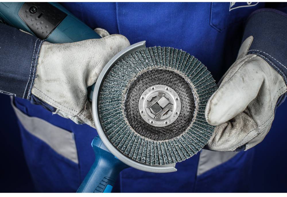 Une personne en vêtements de travail bleus tient une meuleuse d'angle avec des gants en cuir. La mise au point est sur le disque de meulage.