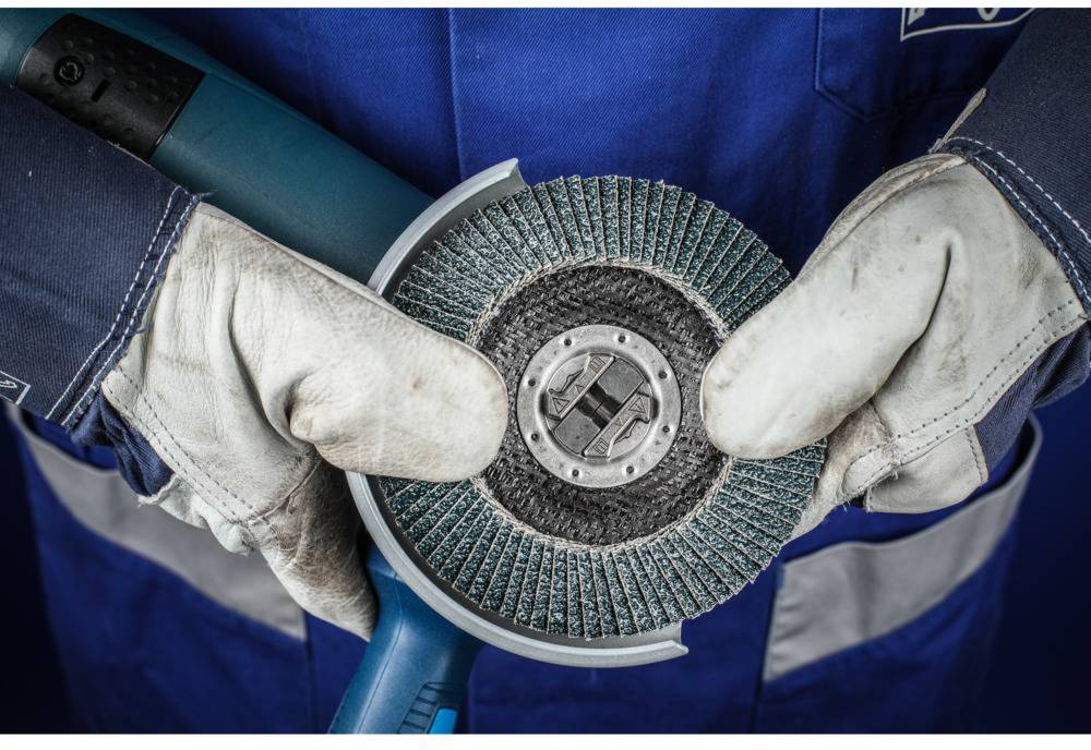 Un ouvrier en vêtements de protection bleus et gants blancs tient une meuleuse électrique à disque.