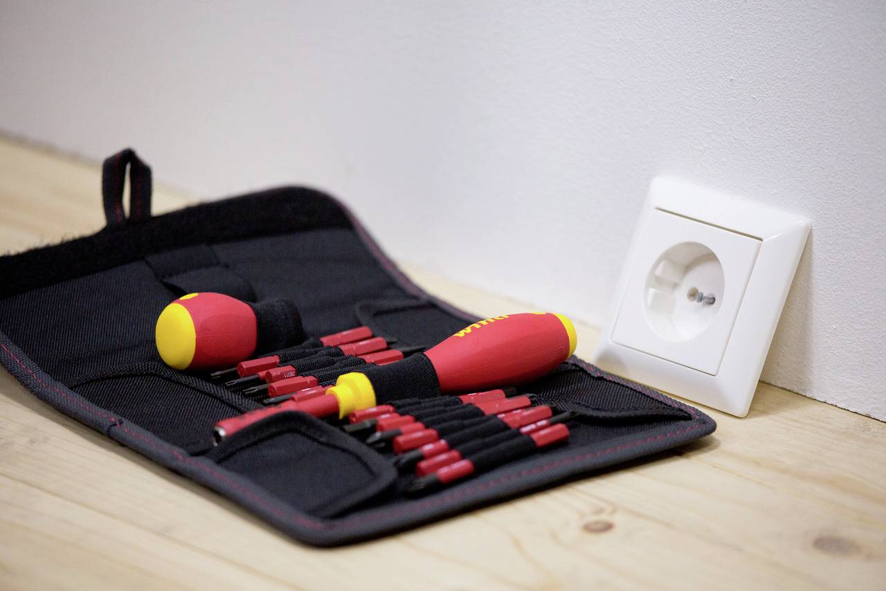Une boîte à outils ouverte est posée à côté d'une prise électrique. Le coffret contient plusieurs tournevis rouges avec des manches jaunes.