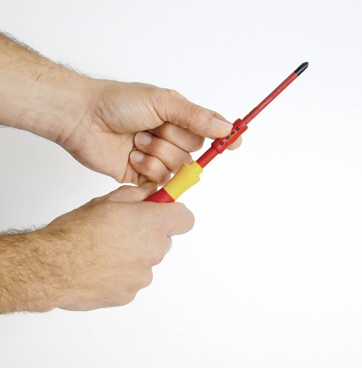 Deux mains tiennent un tournevis isolé avec une poignée rouge et jaune, adapté aux travaux sur installations électriques.