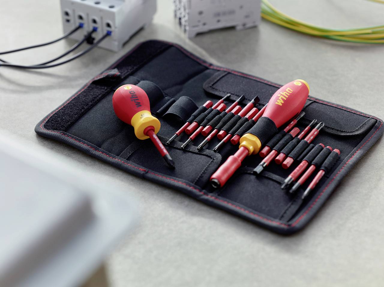 Ensemble d'outils comprenant différents tournevis et embouts dans une pochette ouverte. Des câbles et des connecteurs sont visibles en arrière-plan.