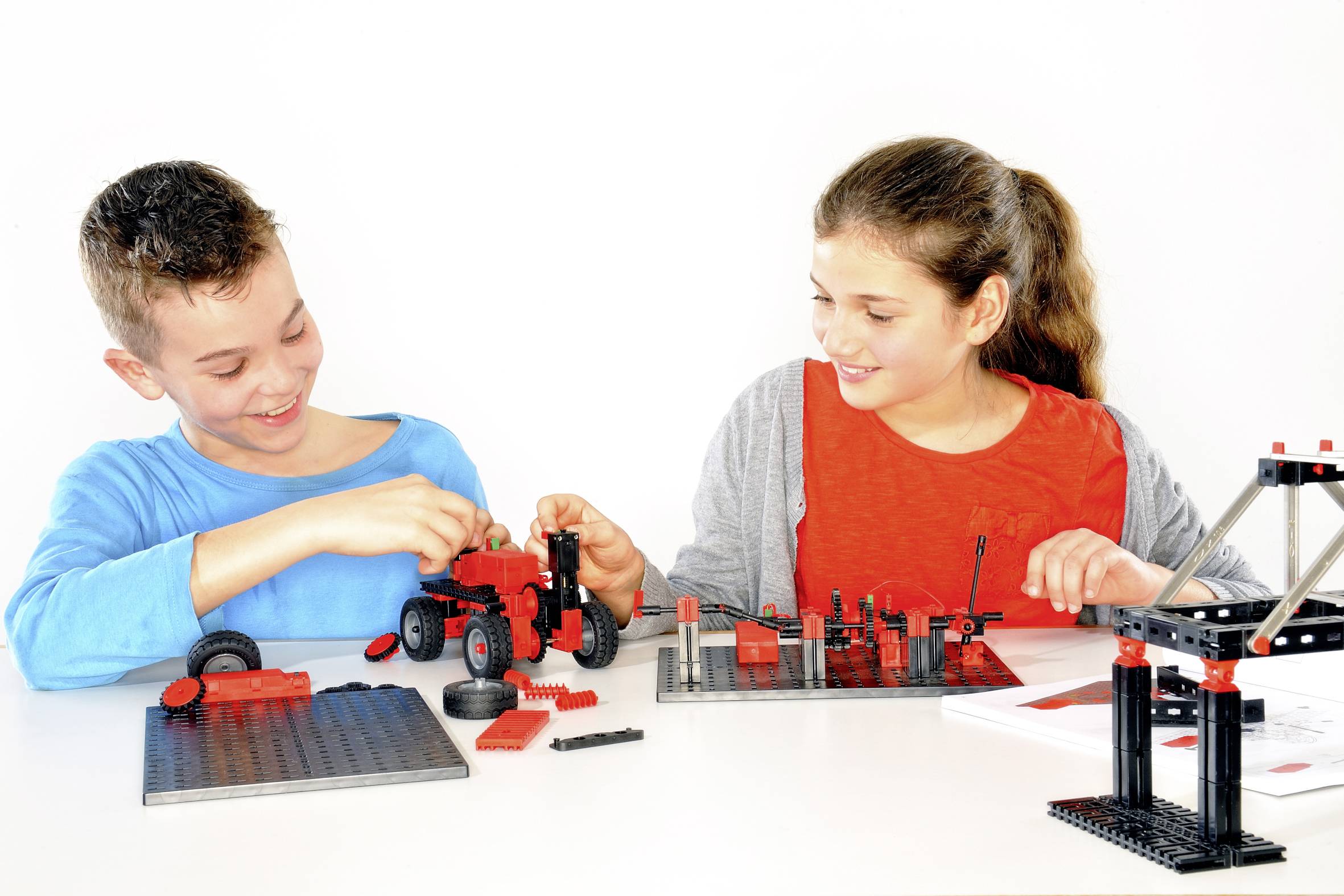 Deux enfants construisent des modèles avec des blocs rouges et noirs, un sourire aux lèvres, autour d'une table. Ils sont complètement absorbés dans leur activité créative.