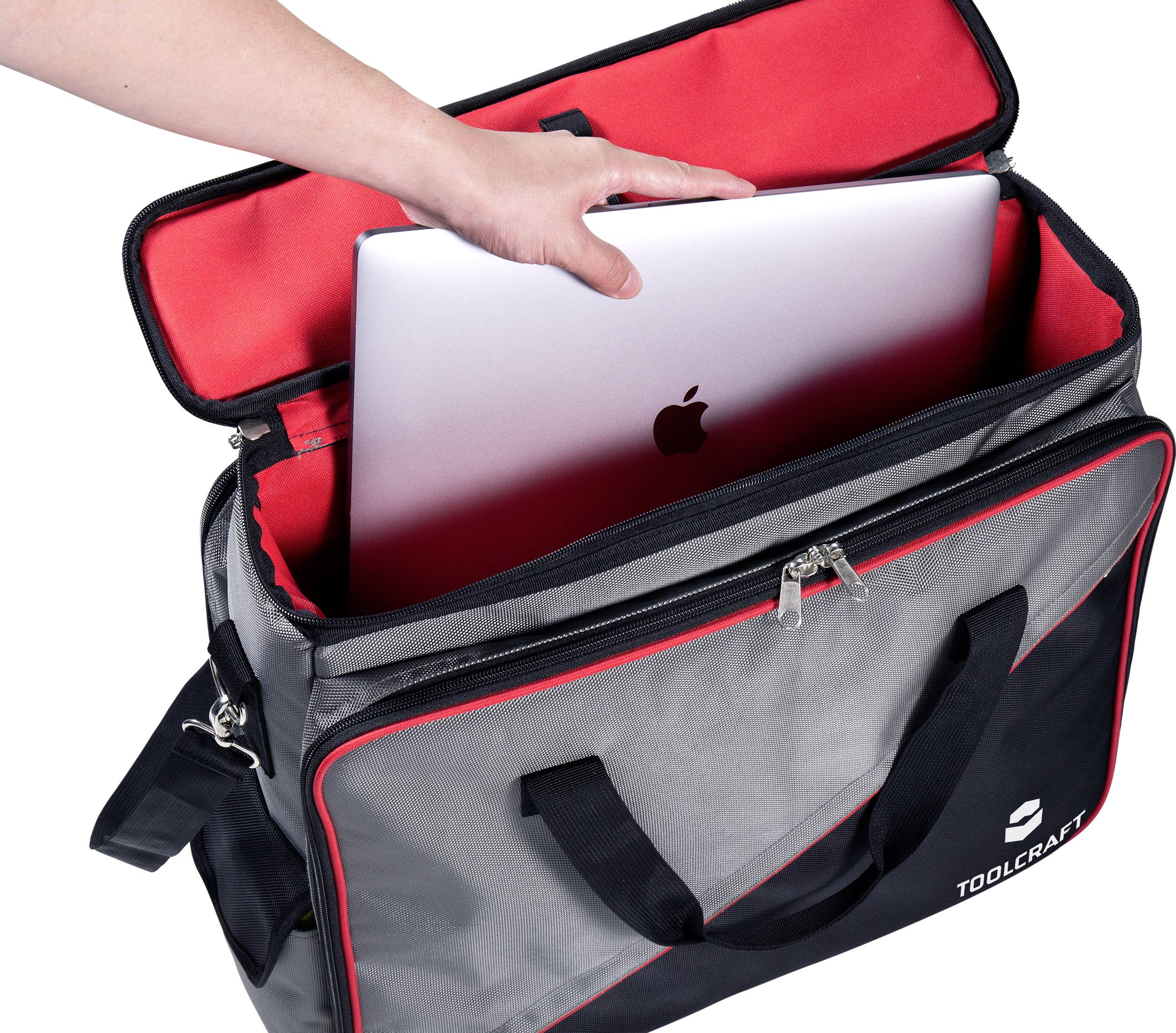 Une personne glisse un ordinateur portable dans un sac ouvert gris et rouge de TOOLCRAFT.