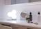 Une étagère de salle de bain avec divers produits de soin, un miroir rond et une lampe hexagonale lumineuse en arrière-plan.