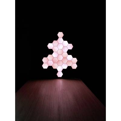 Panneaux lumineux en forme de sapin, composés de modules hexagonaux, placés sur une table et produisant une lumière douce et indirecte dans un environnement sombre.