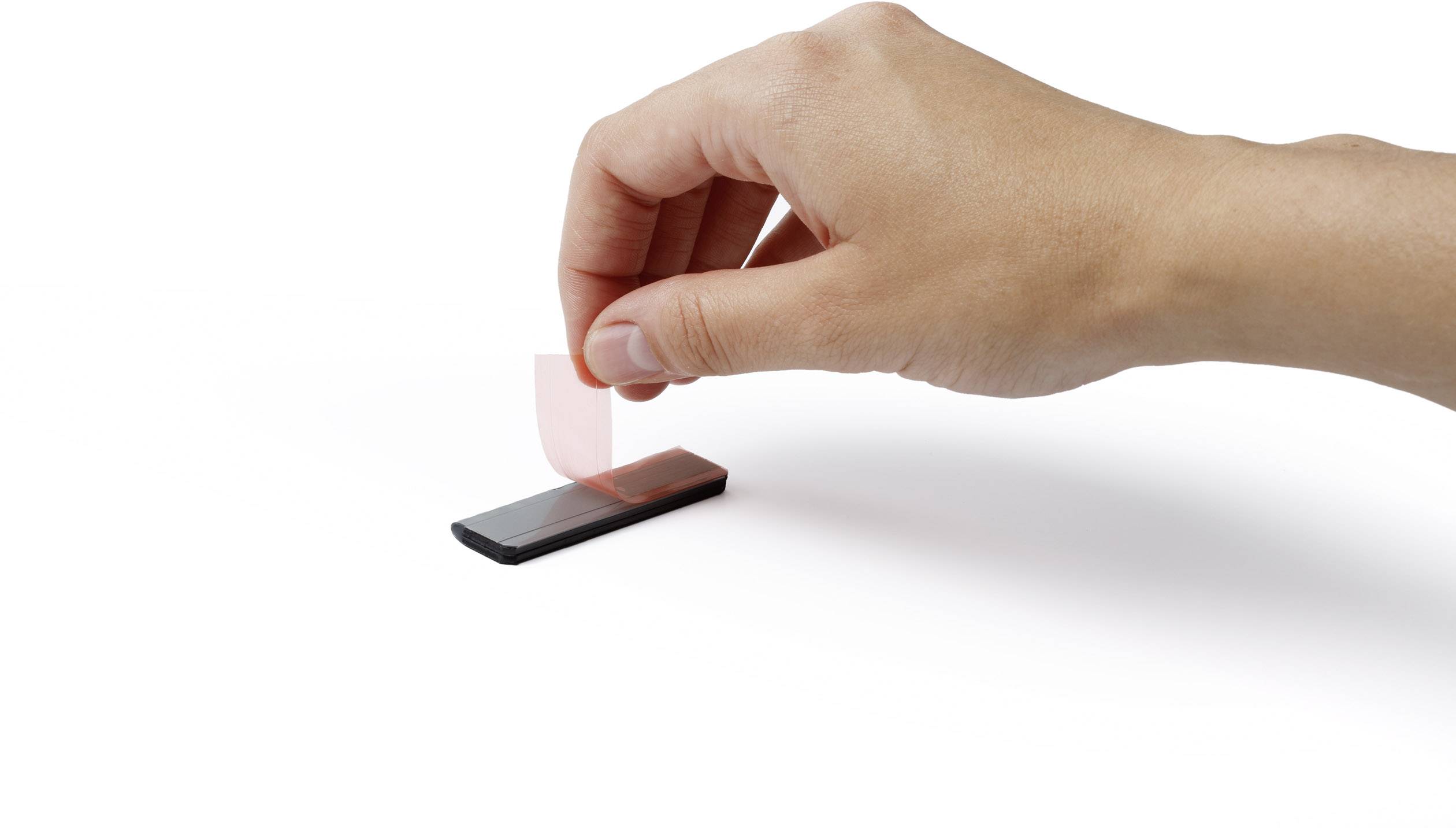 Une main retire un morceau de ruban adhésif d'un rectangle noir, démontrant possiblement une technique ou une application.
