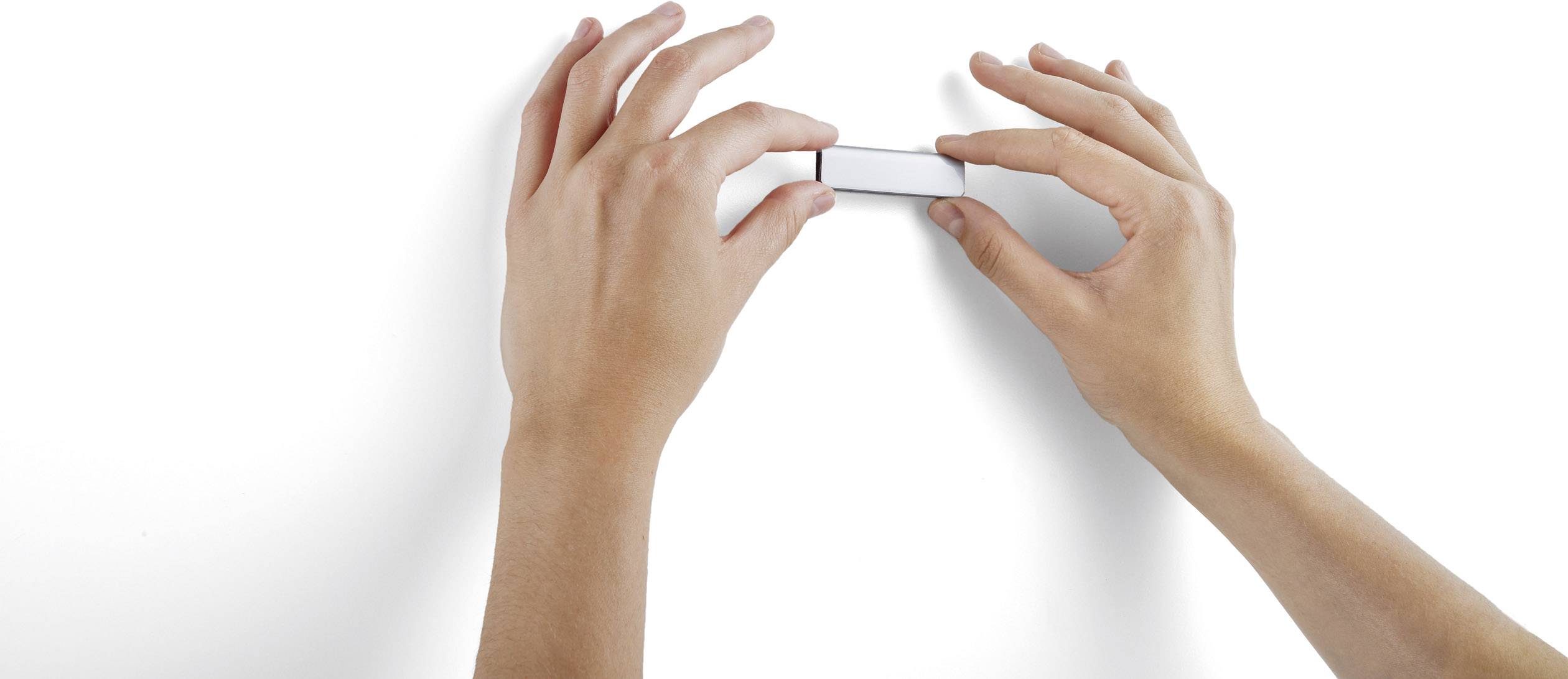 Deux mains tiennent une gomme rectangulaire blanche devant un fond blanc.