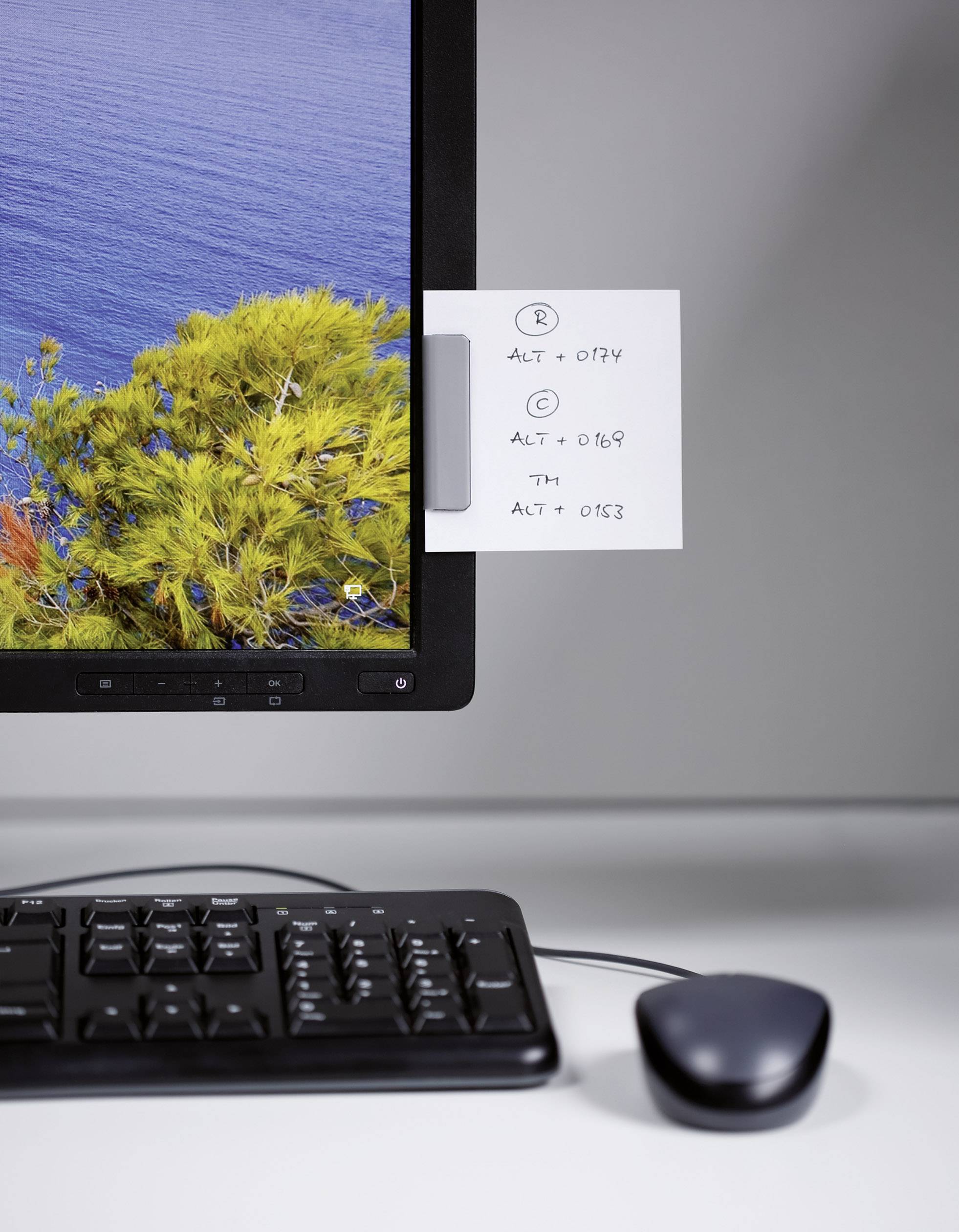 Sur un bureau, il y a un écran d'ordinateur avec un post-it collé dessus, un clavier et une souris. Le post-it montre des combinaisons de touches ALT.