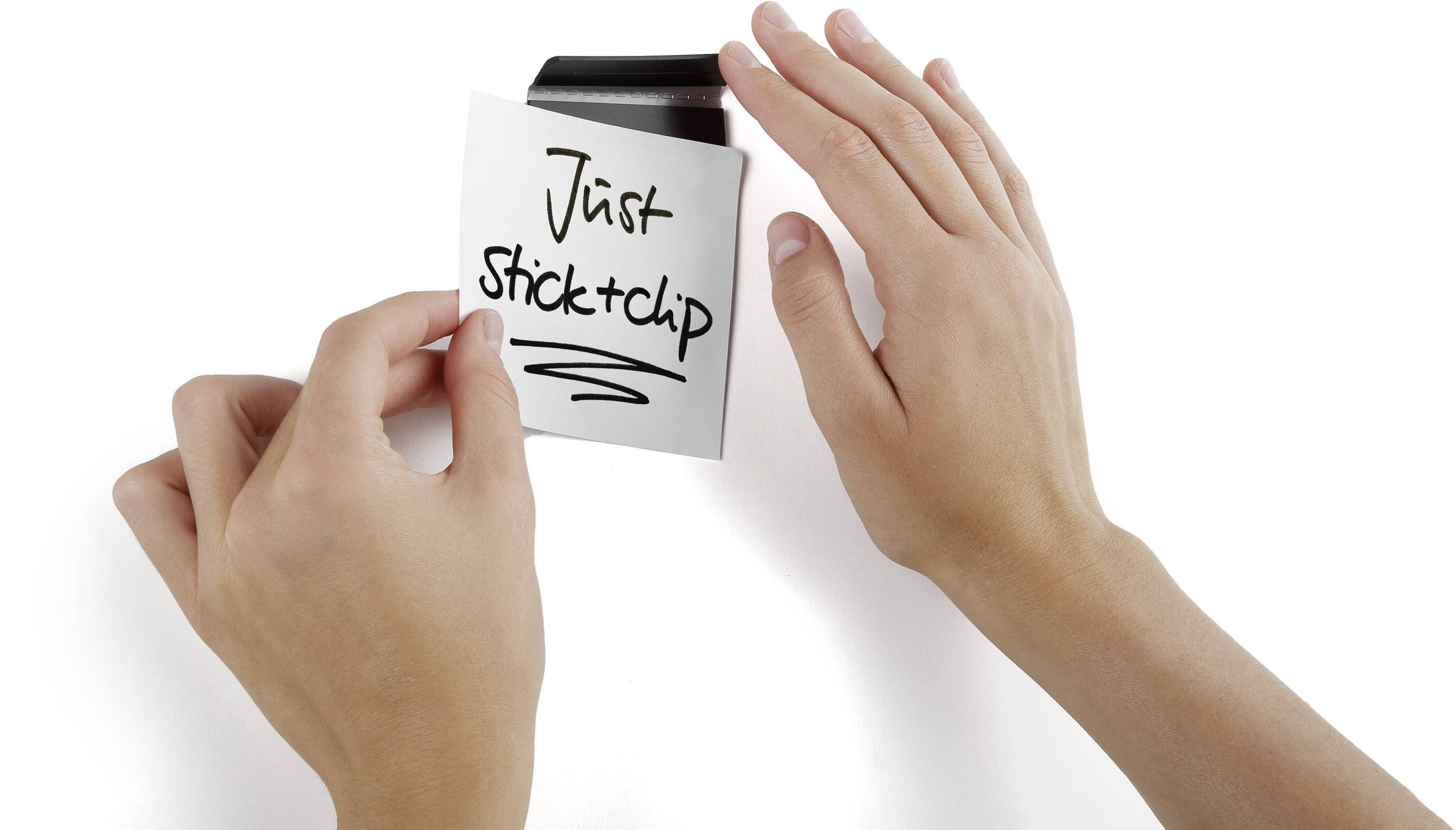 Deux mains tiennent un morceau de papier portant l'inscription 'Just stick it' sur une surface noire.