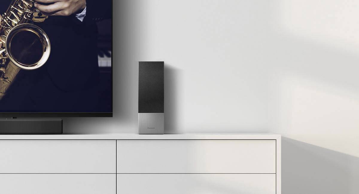 Un buffet blanc avec un haut-parleur noir posé dessus, à côté d'un téléviseur à écran plat montrant un saxophoniste.