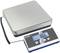 Balance électronique avec affichage numérique indiquant '0,00 kg'. De forme plate, rectangulaire, avec des touches de contrôle pour la tare, la mise en attente et le changement d'unité.