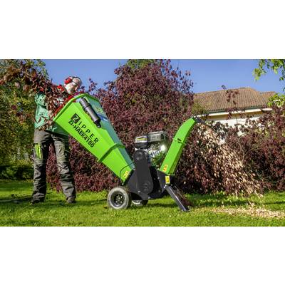 Une personne utilise un broyeur vert et noir à l'extérieur. Des branches sont introduites tandis que des copeaux de bois sont éjectés sur le côté.