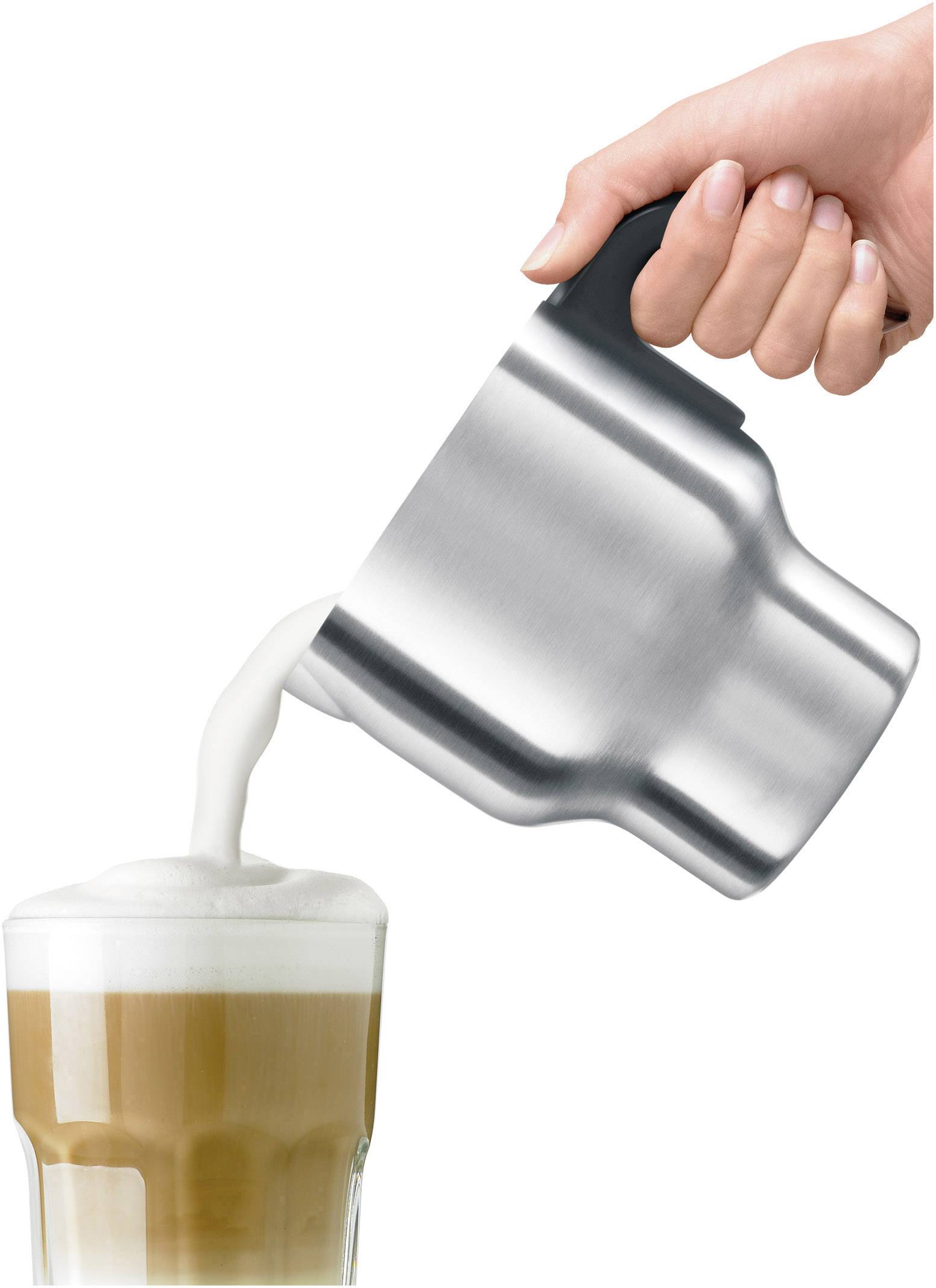 Une main verse de la mousse de lait d'une cruche en argent dans un verre de café, créant un motif en couches.