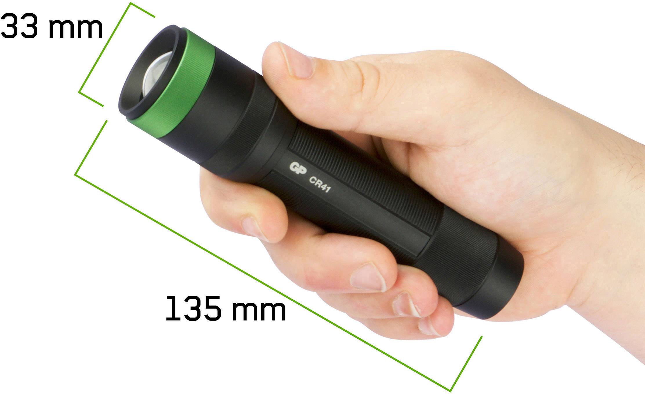 Une main tient une lampe de poche noire avec une bordure verte. Les dimensions sont de 135 mm de longueur et 33 mm de diamètre.