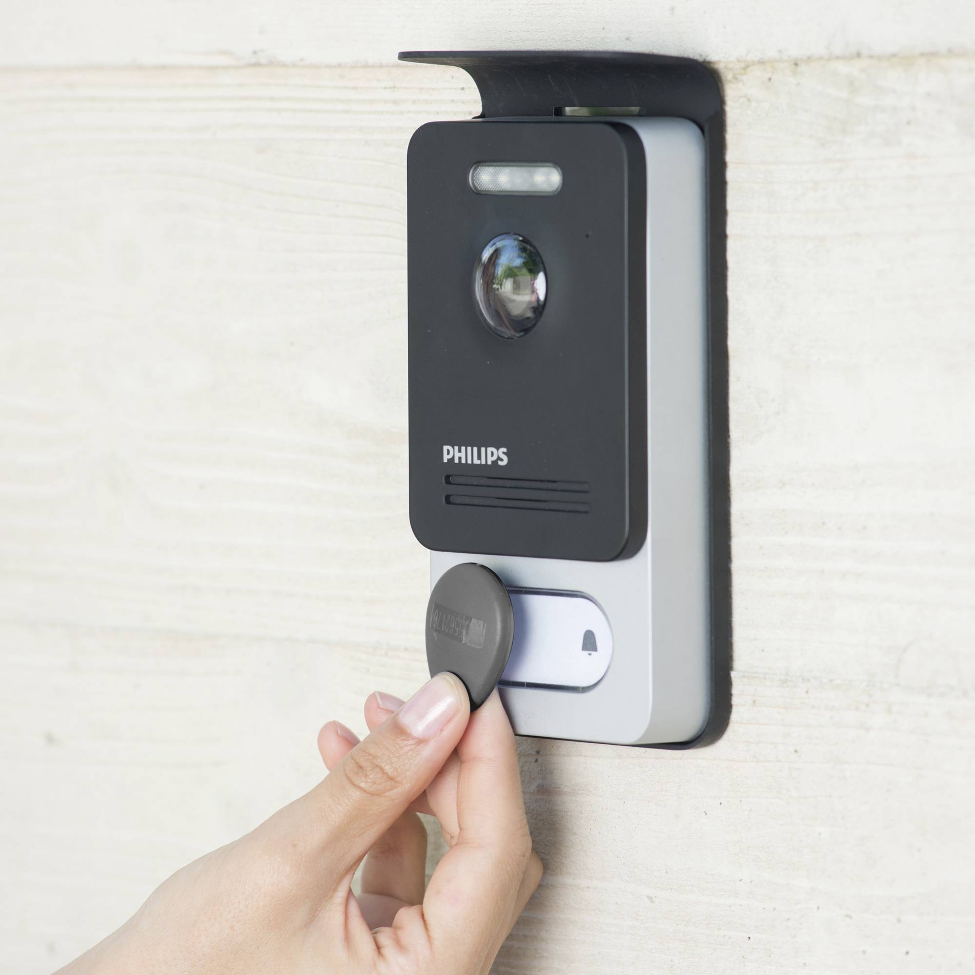 Une main approche un jeton rond d'un serrure électronique Philips sur un mur pour accorder l'accès.