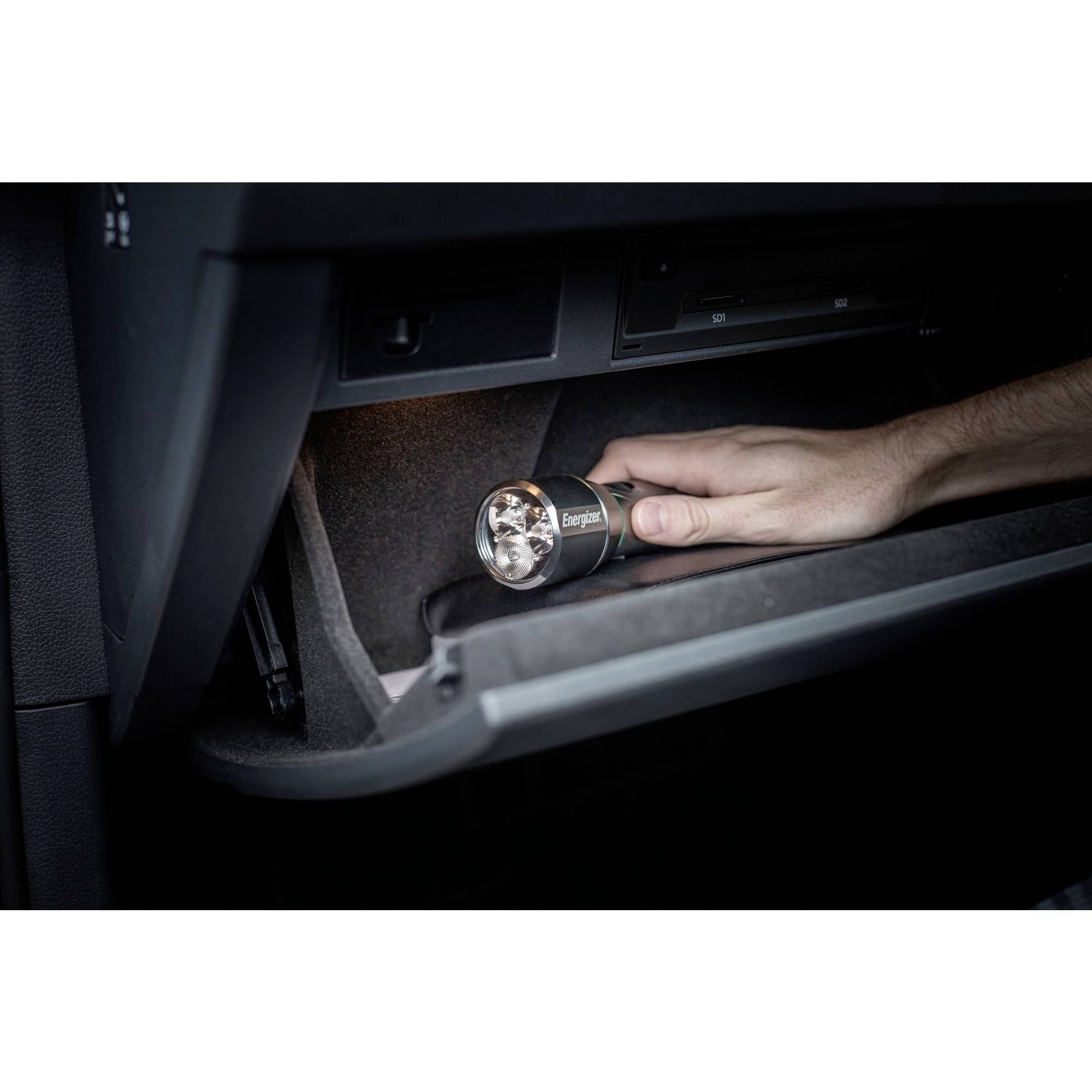 Une main tient une lampe de poche dans la boîte à gants ouverte d'une voiture et éclaire l'intérieur.