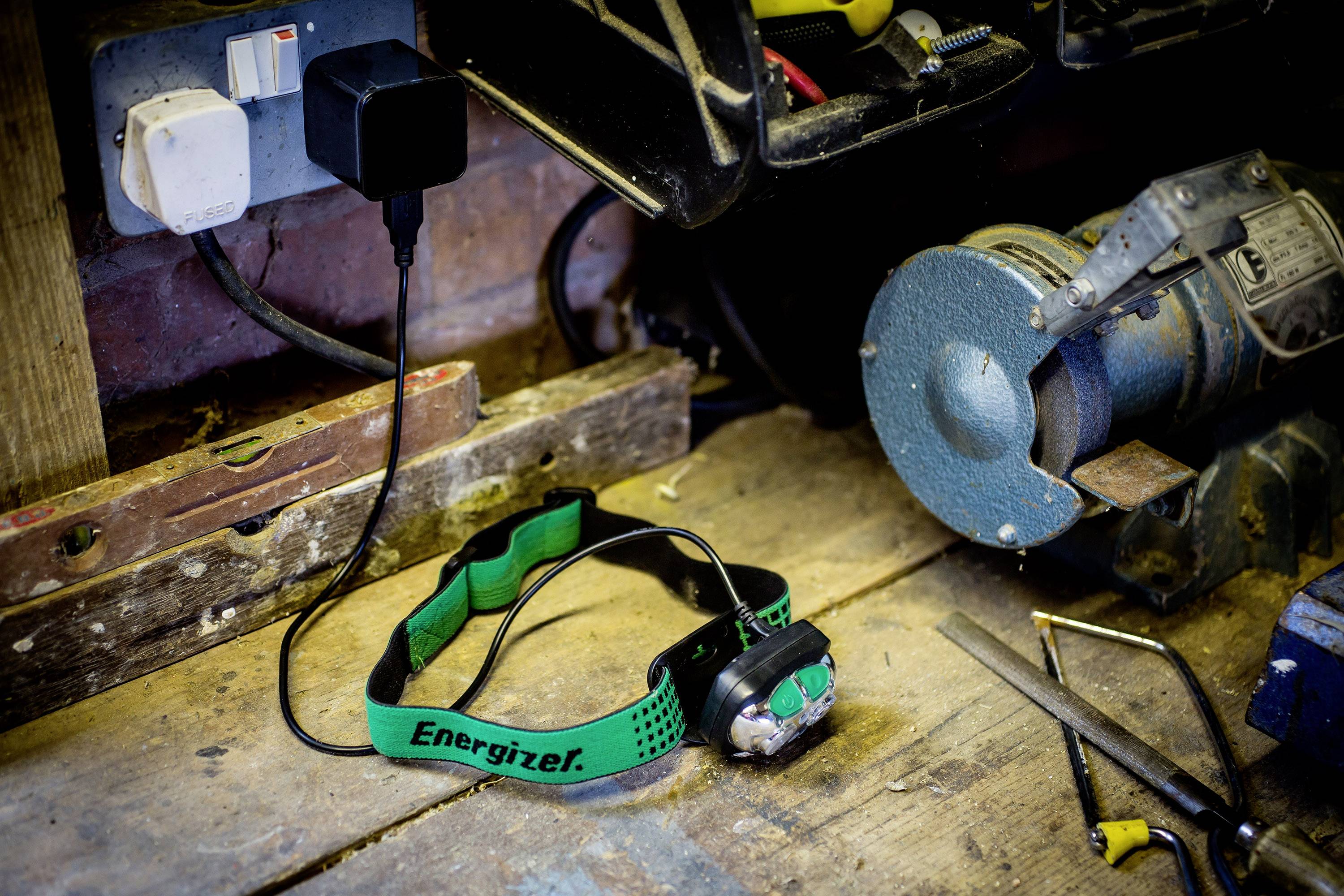 Établi de travail avec chargeur connecté, lampe frontale portant l'inscription 'Energizer', meuleuse et outils posés en arrière-plan.