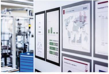Deux rangées de graphiques et de diagrammes sur un mur. À gauche, on distingue un environnement industriel flou.