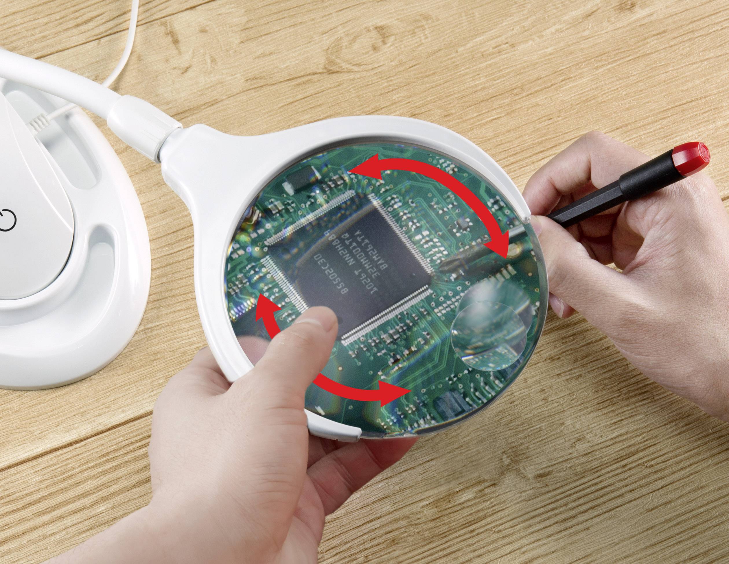 Une personne examine un circuit imprimé vert à l'aide d'une loupe et d'un stylo. Des flèches rouges indiquent la direction d'un circuit.