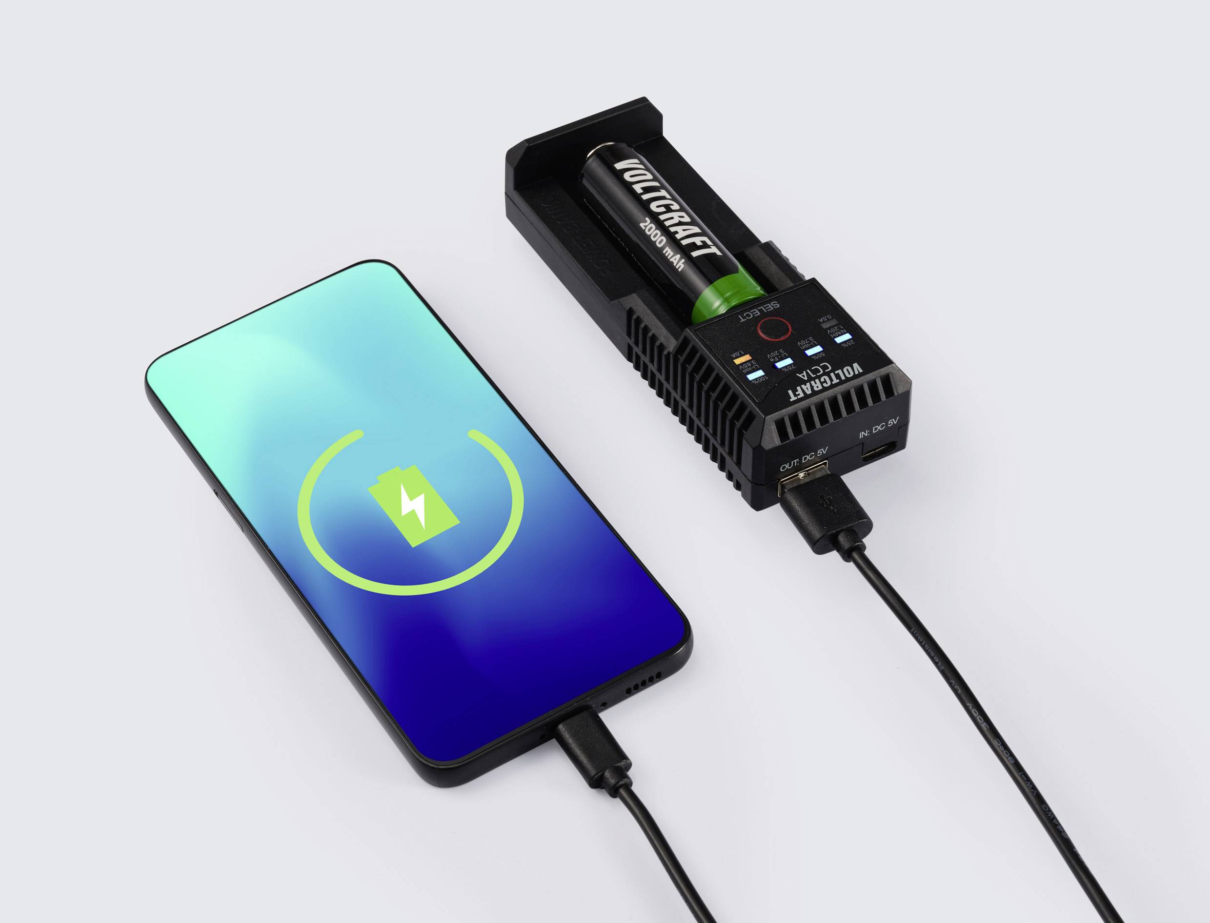 Un smartphone est en train de se charger, à côté se trouve un chargeur de batterie avec une batterie. Les deux appareils sont reliés par des câbles.