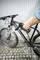 Une personne nettoie un vélo tout-terrain boueux à l'aide d'un nettoyeur haute pression sur un sol pavé devant un mur gris.