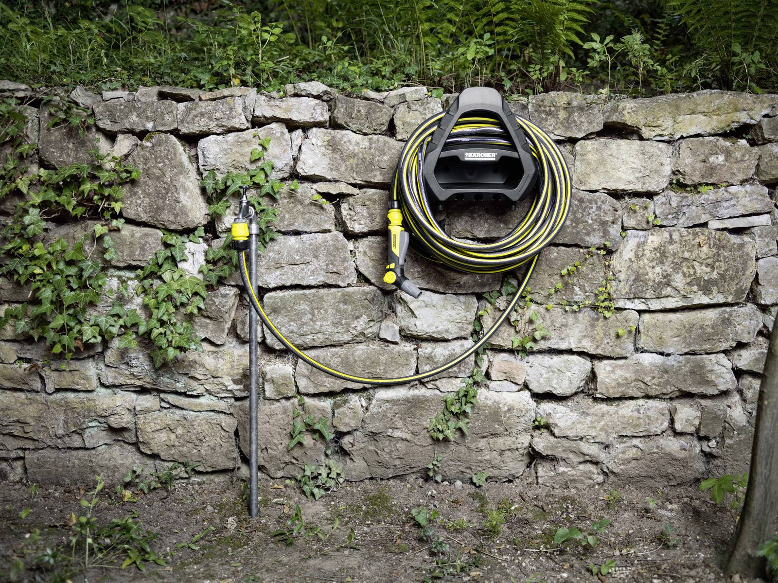 Un enrouleur de tuyau d'arrosage fixé à un mur en pierre, avec un tuyau jaune et noir enroulé et un robinet.