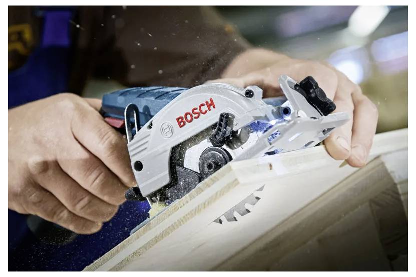 Une personne utilise une scie circulaire Bosch pour couper une planche en bois, démontrant un travail du bois précis dans un atelier.