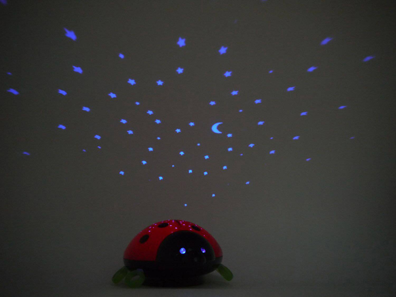 Veilleuse coccinelle qui projette des étoiles bleues et des motifs de lune sur un mur sombre, créant une atmosphère apaisante dans la pièce.
