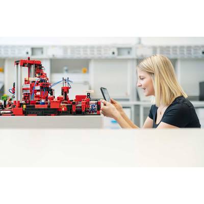 Une femme travaille avec concentration à une table, un smartphone à la main, à côté d'elle se trouve un modèle complexe construit en briques rouges dans un espace moderne.