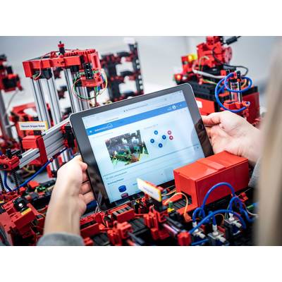 Une personne tient une tablette dans ses mains, affichant la commande d'un système robotique complexe rouge avec des câbles et des pièces mécaniques.