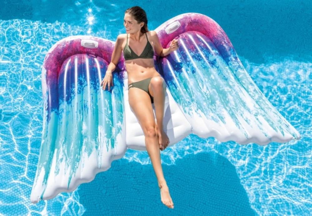 Femme allongée sur un matelas pneumatique avec des ailes d'ange dans une piscine, atmosphère estivale, détente dans l'eau par temps ensoleillé.
