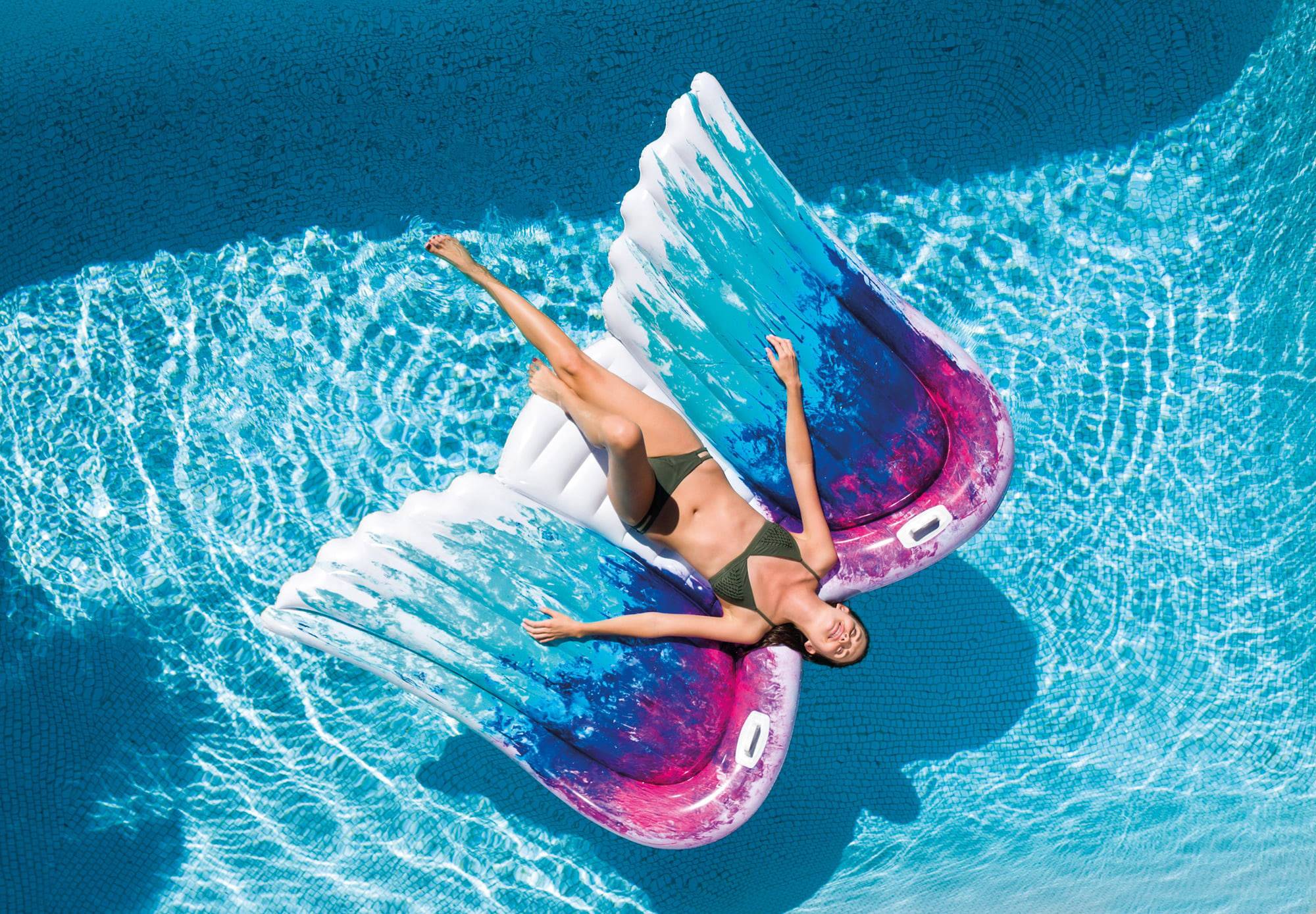 Une personne se détend sur un matelas pneumatique coloré en forme d'ailes dans l'eau claire et bleue de la piscine.
