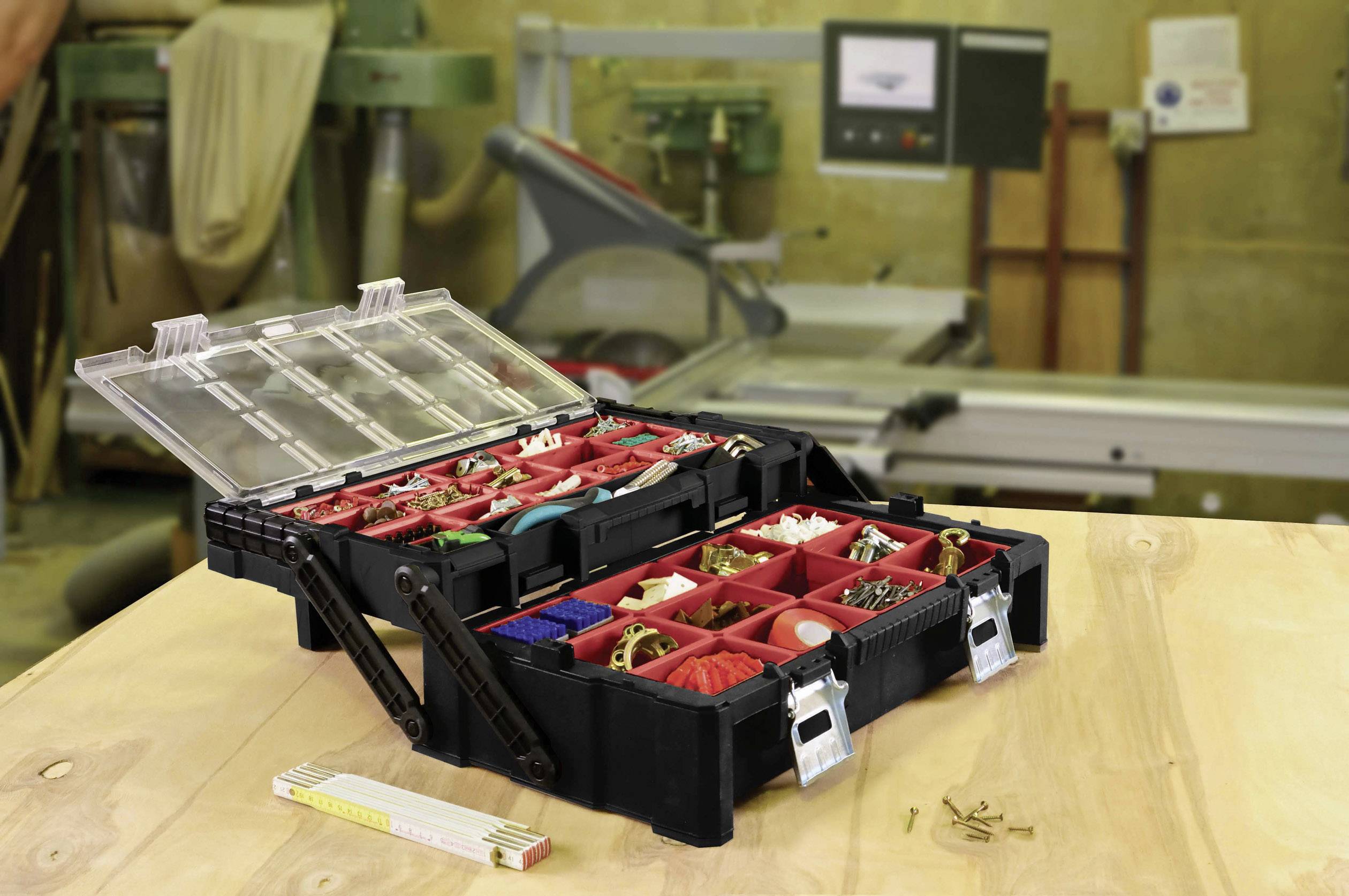 Boîte à outils avec des compartiments ouverts remplis de vis, de clous et de petites pièces sur une table d'atelier. Arrière-plan : machines et outils.