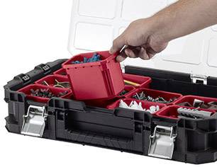 'Une main ouvre un coffret à outils noir avec un tiroir rouge rempli de différentes vis et outils.'