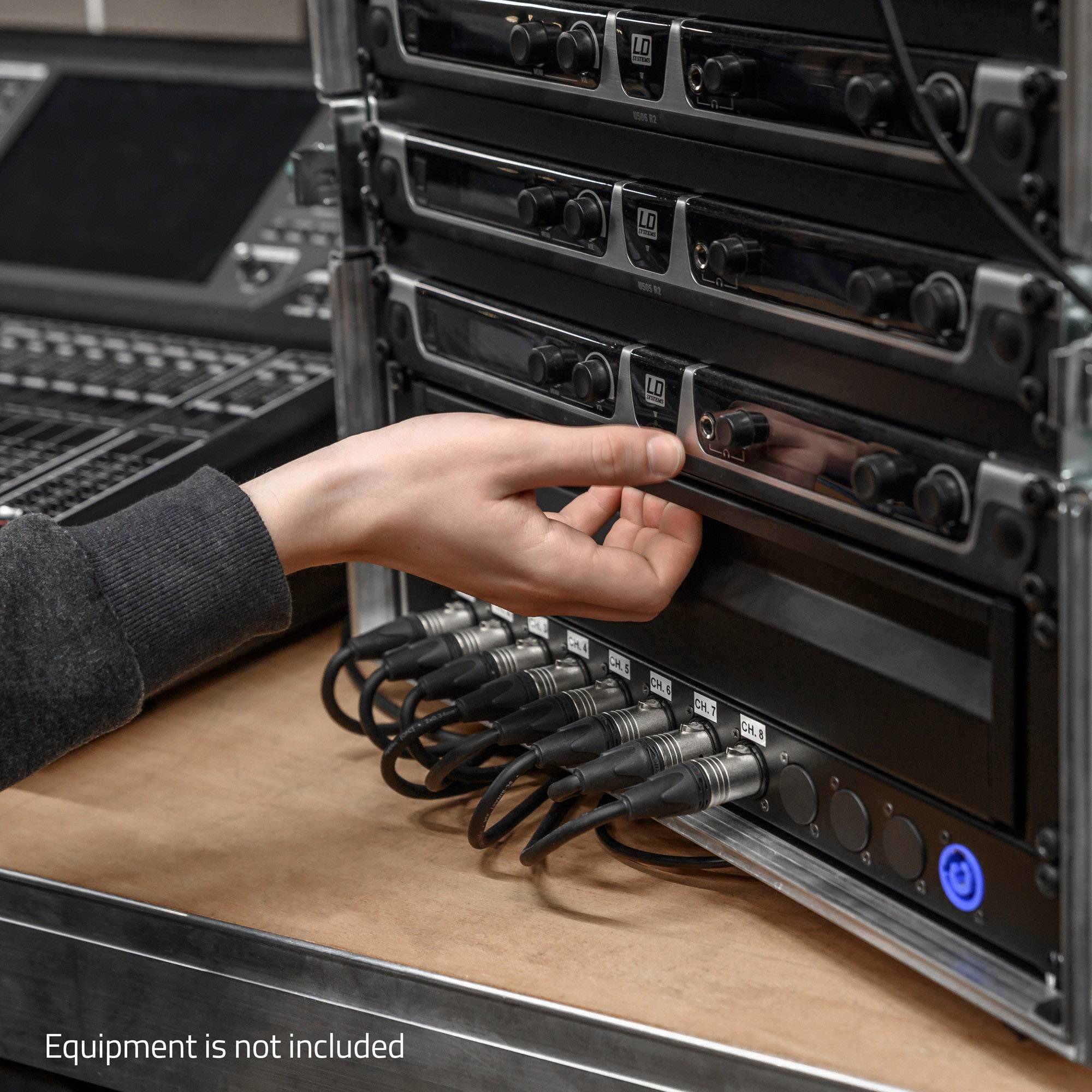 Une main manipule un appareil audio fixé dans un rack. Plusieurs câbles sont connectés en bas. Texte : 'Équipement non inclus'.
