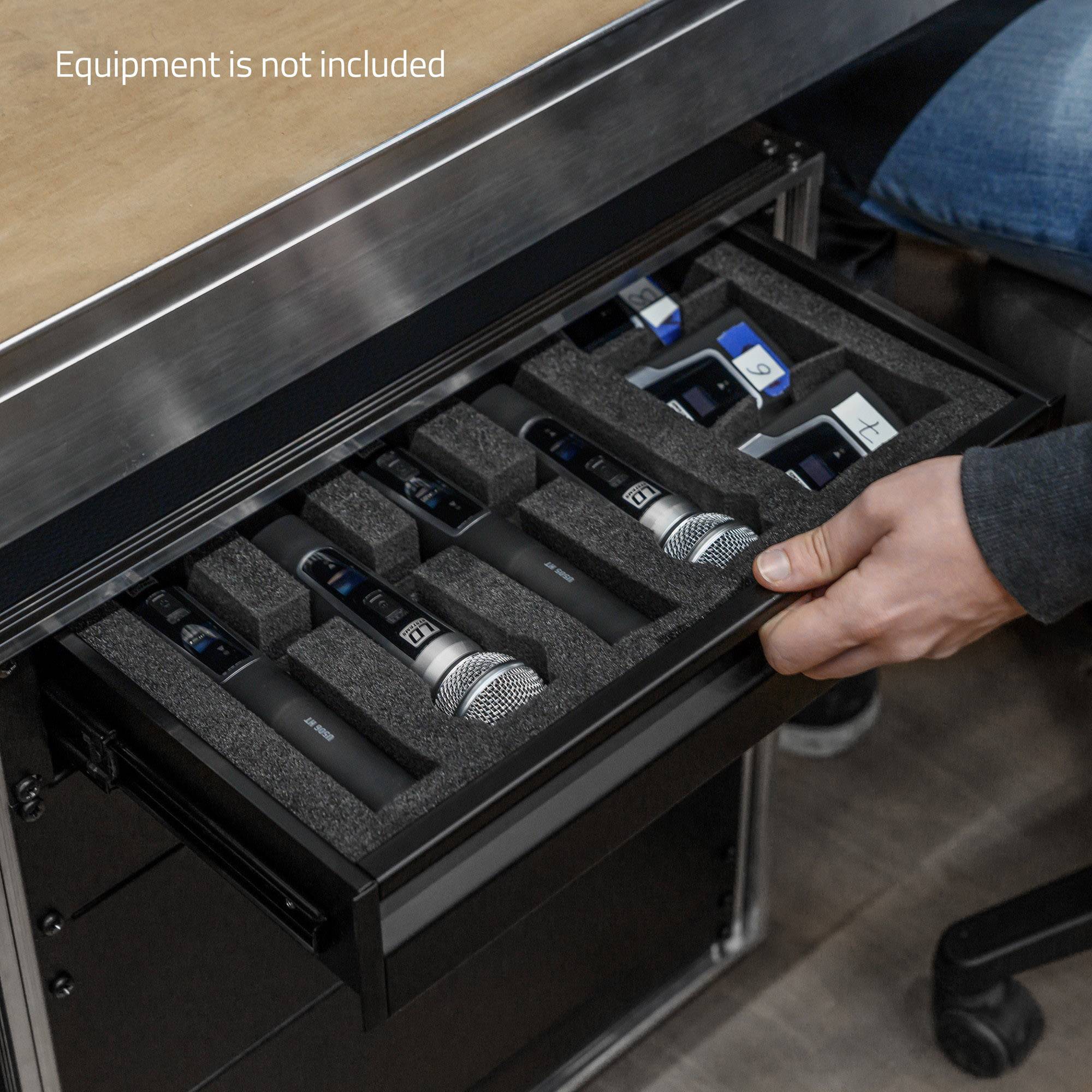 Une main saisit un microphone dans un tiroir compartimenté et rembourré, placé sous une table. Au-dessus est inscrit « L'équipement n'est pas inclus ».