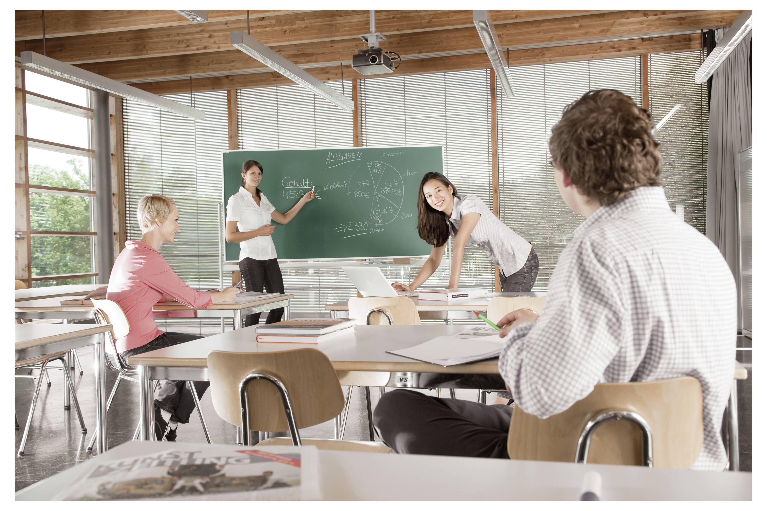 Les étudiants dans une salle de classe regardent un enseignant qui pointe vers un tableau noir pendant un cours.