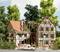Une maquette d'une ancienne maison à colombages avec un toit endommagé. Devant se trouvent des figurines miniatures portant des uniformes rouges et une ambulance.
