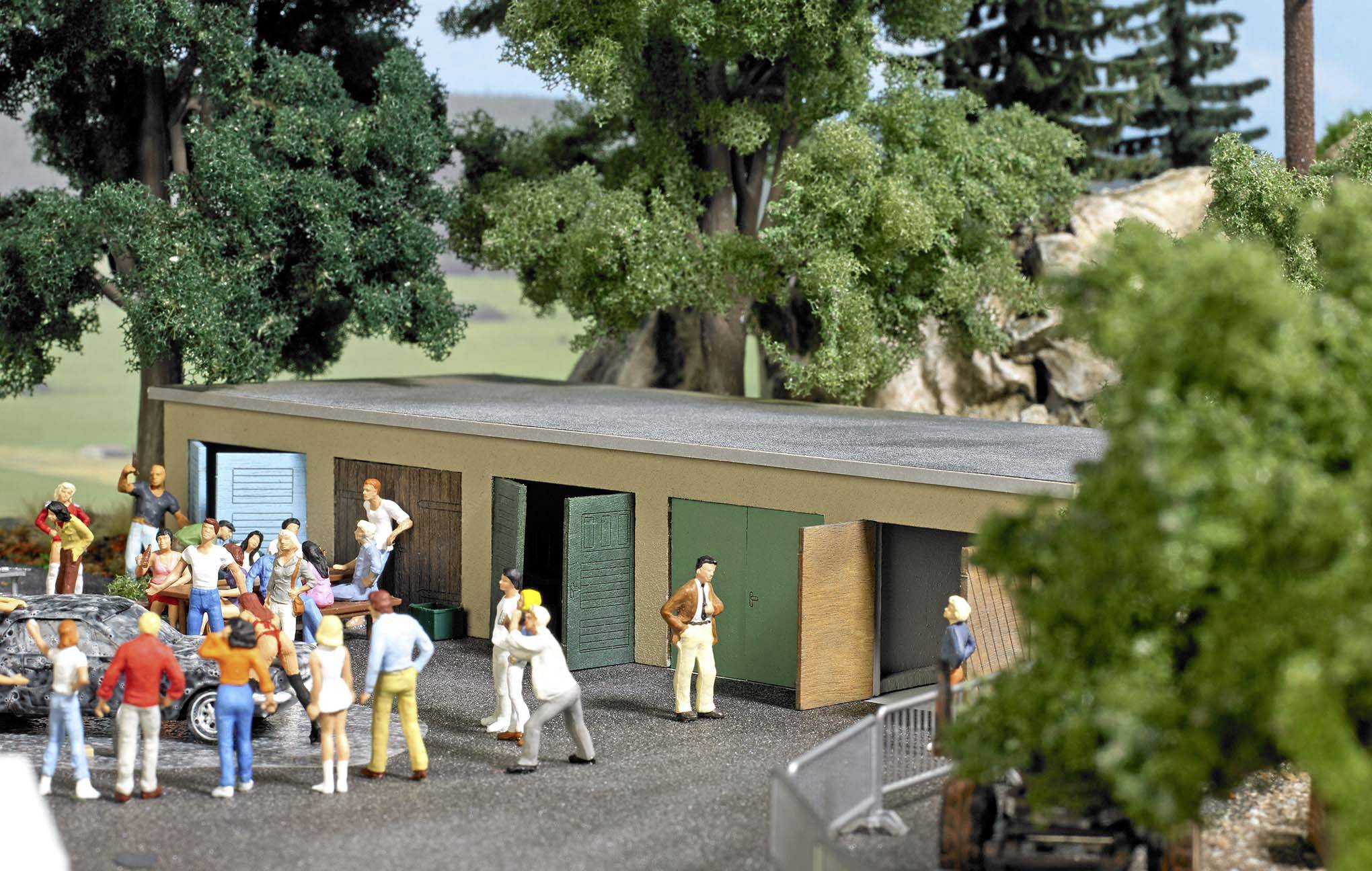 Un modèle miniature représente un groupe de personnes devant des garages dans une zone boisée. Les individus semblent animés, comme s'ils étaient en train de célébrer.