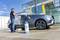 Une personne lave une voiture argentée avec un nettoyeur haute pression dans une station de lavage. La voiture est recouverte de mousse.