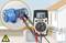Un multimètre mesure une tension de 230V sur une pompe électrique dans une maison. Symbole de sécurité indiquant un danger électrique.