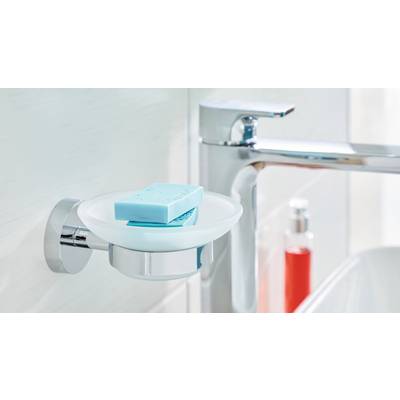 Un savon bleu repose dans un porte-savon à côté d'un robinet moderne dans la salle de bain. À l'arrière-plan, un récipient contenant un liquide rouge est visible.