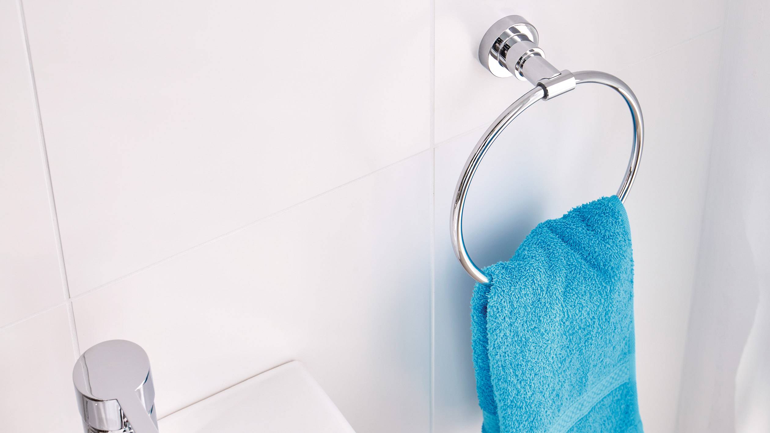 Une serviette bleue est suspendue à un porte-serviette rond en argent, fixé à un mur blanc de salle de bain.