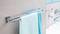 Un porte-serviettes avec deux serviettes bleues est accroché au mur d'une salle de bain. En arrière-plan, on peut voir un tube de dentifrice et un lavabo.