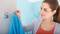 Une femme accroche une serviette bleue à un crochet dans la salle de bain. Elle porte un haut rouge et un cardigan gris.