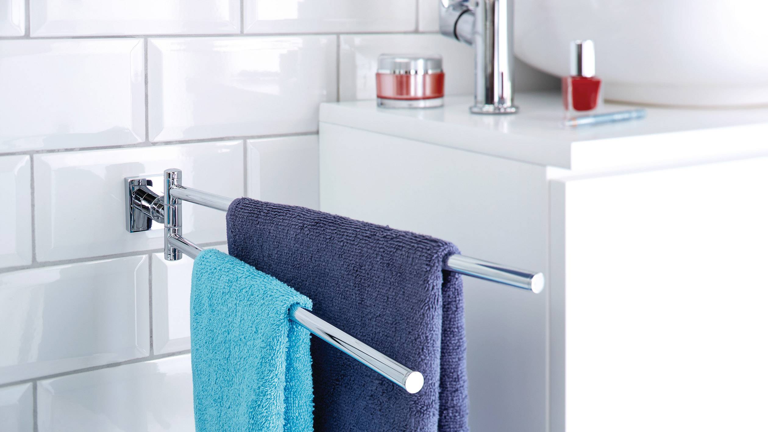 Deux serviettes, l'une bleue, l'autre gris foncé, sont suspendues côte à côte sur un porte-serviettes double dans la salle de bain.