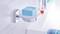 Une savonnette bleue dans un support fixé au mur d'une salle de bain, à côté d'un lavabo avec une serviette et un distributeur rouge en arrière-plan.