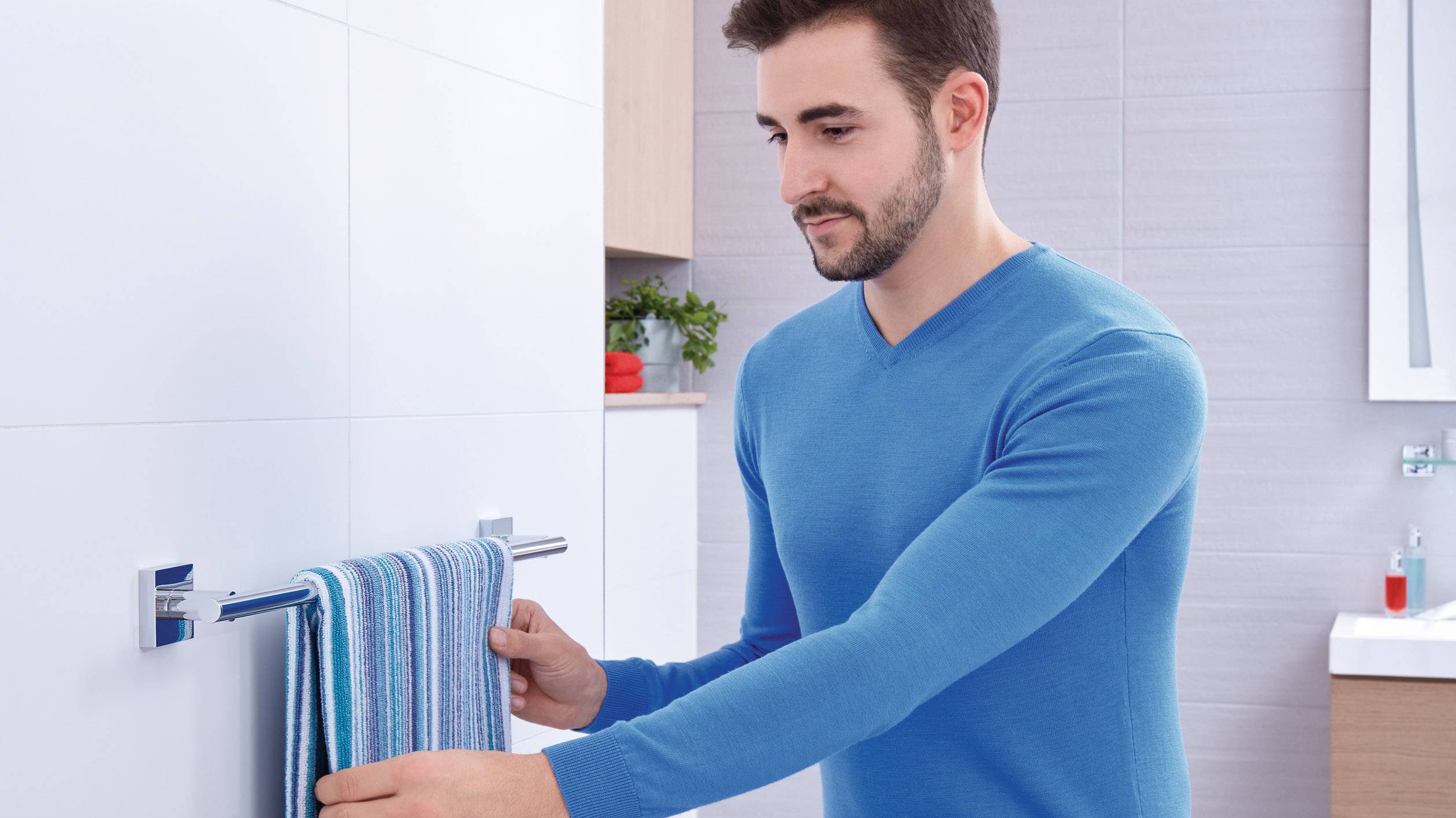 Un homme portant un pull bleu accroche une serviette rayée dans une salle de bain au design moderne.