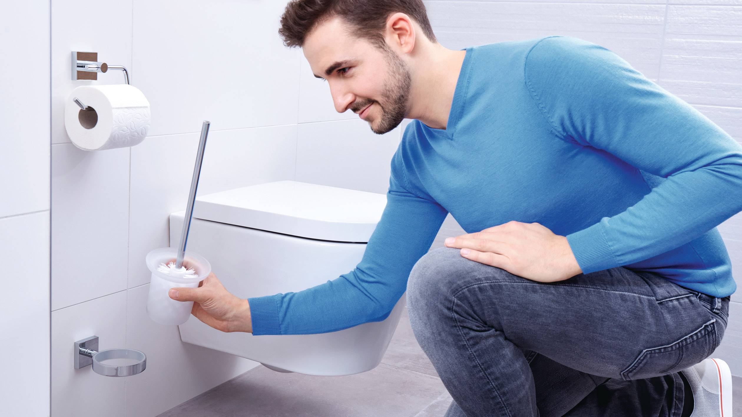 Un homme vêtu de bleu nettoie une cuvette de toilettes avec une brosse dans une salle de bain moderne.
