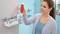 Une femme dans la salle de bain place une bouteille rouge sur une étagère en argent fixée au mur. D'autres articles de toilette sont également présents sur l'étagère.